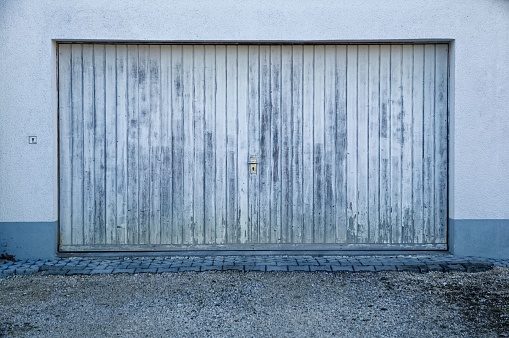 An aged metallic garage door that is beginning to peel and a gravel driveway with a weathered stone