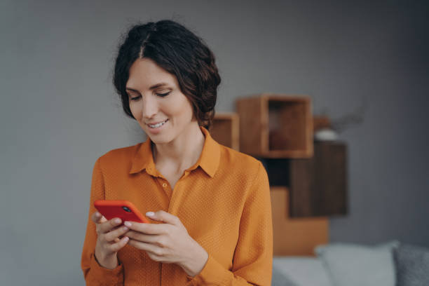 istock Young smiling hispanic lady holding smartphone, looking at screen with smile and texting sms 1479427555