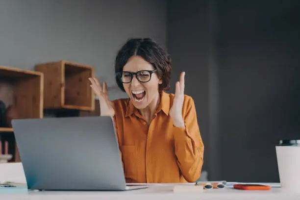 Mad Italian businesswoman shouting in distress from hopelessness while working from home, exhausted home office employee in desperate situation without solution, unable to cope with nervous breakdown
