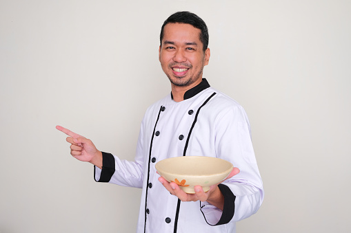 Asian Chef smiling happy and pointing to the right side while showing empty bowl