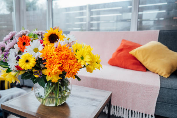 istock Vase with huge multicolor various mixed flower bouquet on the coffee table with background of modern cozy light conservatory room with couch sofa and bright cushions. Fresh flowers in interior. 1479427750