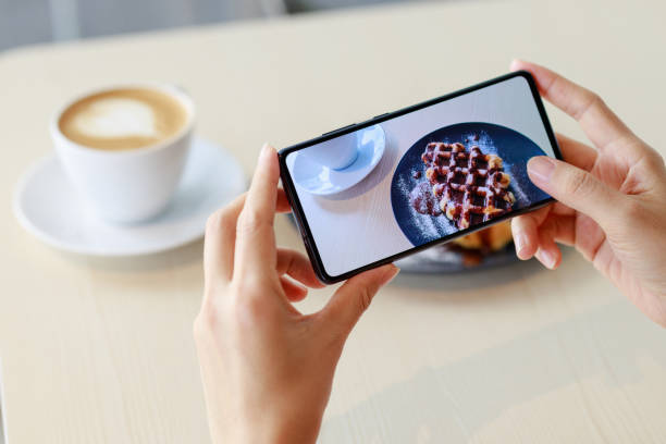 una food blogger sta usando il suo smartphone per catturare un'immagine della sua colazione e del suo caffè, che ha intenzione di condividere sui social media. - catturare unimmagine foto e immagini stock