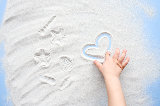 Child plays with sand, draws a heart.