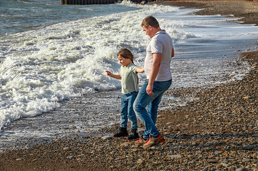 The concept of a friendly family. Father and daughter play on the beach in the afternoon. Father and daughter are running on the waves of the surf.