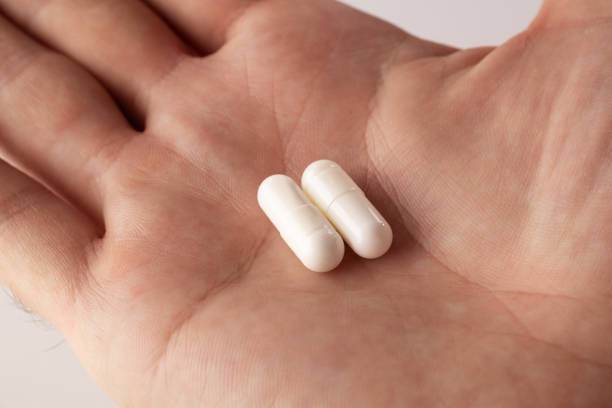 istock Male hand holding two pills in hand on grey background. 1479434956