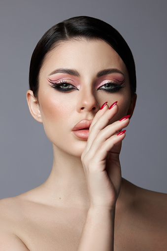 Beauty portrait of a woman, pink eye shadow makeup, arrows and long eyelashes. Brunette woman, red nail polish, natural cosmetics