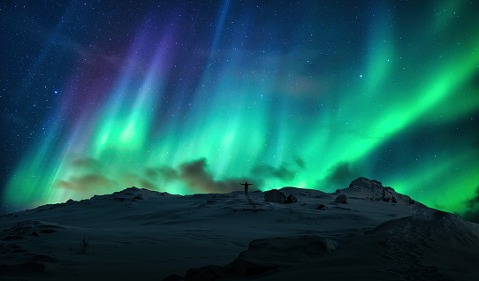 Fantastic Aurora borealis, Northern lights over silhouette cheerful man on top of mountain in arctic circle at Norway