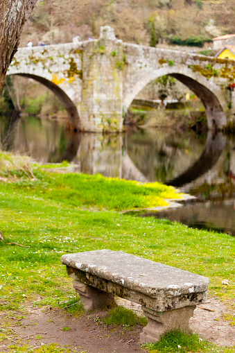 Allariz ancient Vilanova stone bridge over Arnoia river, set in XIII century, Stone bench in the foreground. Allariz village, Ourense province, Galicia, Spain. Idyllic monument close-up view.