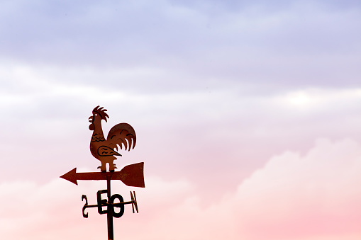 Close up of weathervane in rooster shape silhouetted on a rooftop, sunset sky in the background with copy space on the right. Allariz, Ourense province, Galicia, Spain.