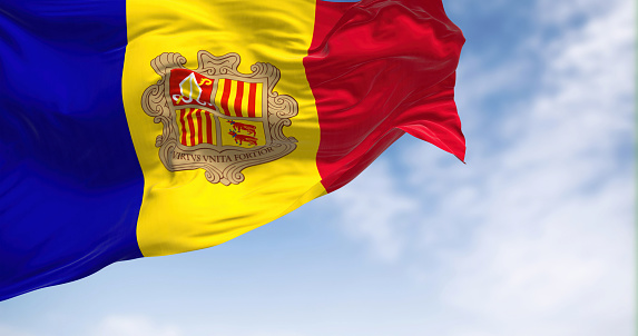 The flag of the Principality of Andorra waving in the wind on a clear day. Vertical blue-yellow-red stripes with coat of arms in center. 3d illustration render. Rippled textile