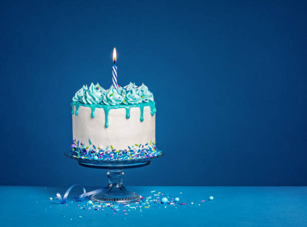 濃い青の背景に白い誕生日のドリップケーキとティールガナッシュと火のついたキャンドル