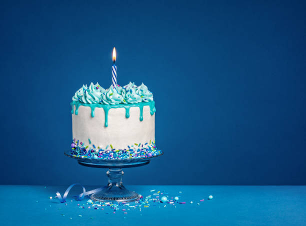 white birthday drip cake with teal ganache and lit candle over dark blue background - copy space single object confetti nobody imagens e fotografias de stock