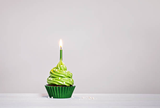 istock Green cupcake with sprinkles and lit birthday candle on a white grey background. 1479449787