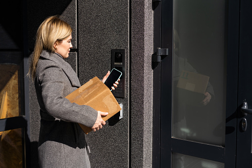 Smart home concept - close up of woman with box use mobile phone to open electronic lock.