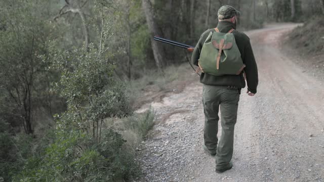 Male hunter holding a gun while walking through the woods with his dog.