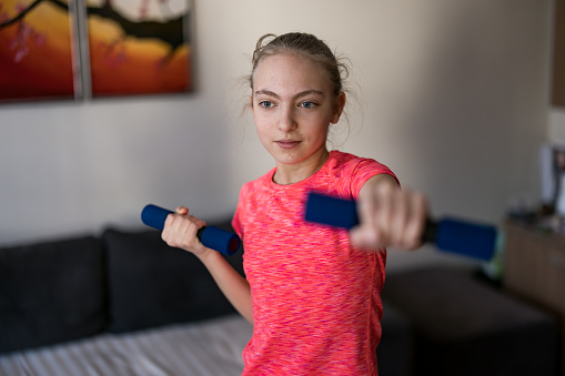 Cute girl exercising with dumbbells at home