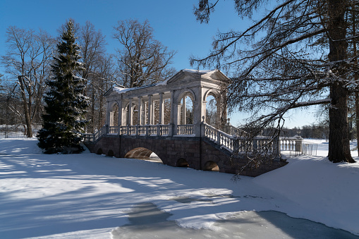Marble bridge on the shore of a Large pond in the Catherine Park in Tsarskoye Selo on a sunny winter day, Pushkin, St. Petersburg, Russia