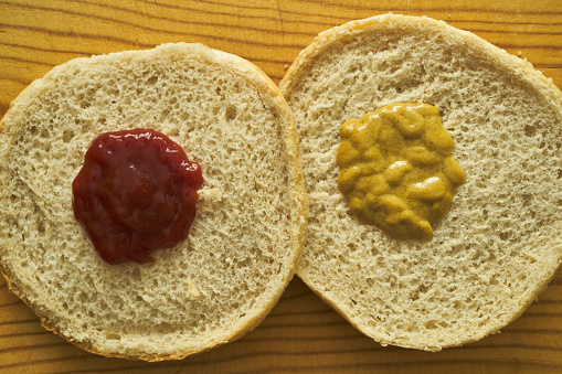 OPEN BURGER BUN WITH KETCHUP IN ONE HALF AND MUSTARD IN THE OTHER HALF