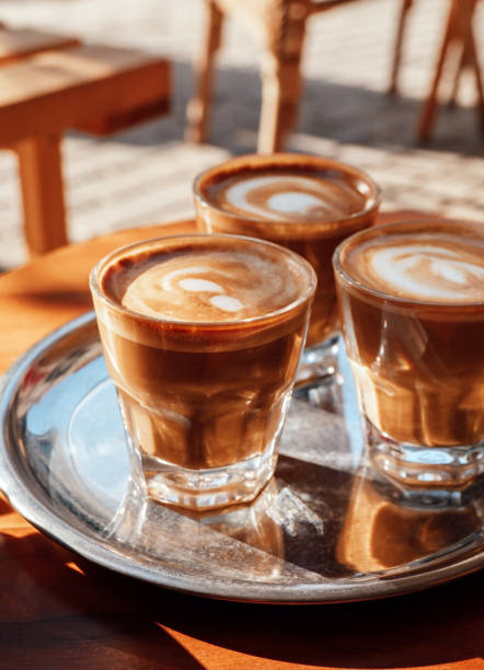enfoque selectivo de tres vasos con café con espuma de leche en una bandeja metálica en cafetería en día soleado. - espresso coffee cream coffee shop fotografías e imágenes de stock