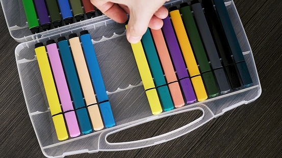 A person puts colored markers into a plastic case.