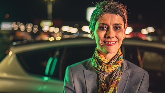 portrait of one senior woman modern mature caucasian female with gray short hair stand in the city at night in front of the car real person copy space waist up