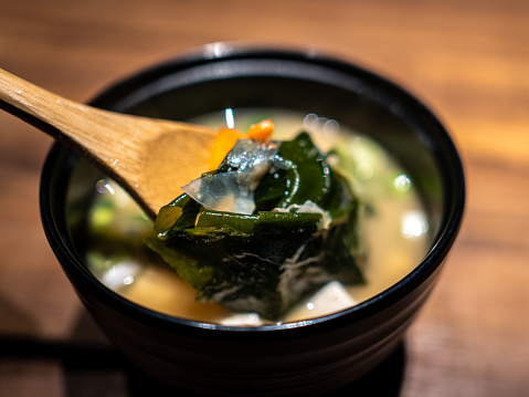 A bowl of Japanese miso soup filled with kelp and ingredients.
