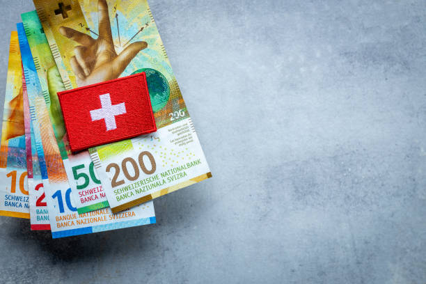 スイスフランの山の上に横たわるスイス国旗、スイスの通貨、ビジネスと金融のコンセプト、コピー用スペース、グレイの背景 - swiss currency ストックフォトと画像