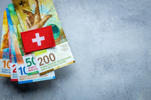 Swiss flag lying on a stack of Swiss francs, Currency of Switzerland, business and finance concept, copy space, gray background