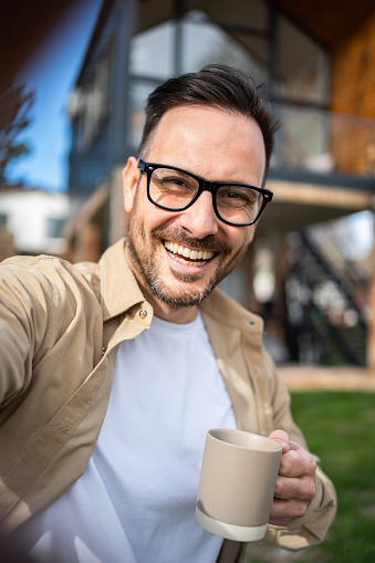 Happy smiling middle aged man standing in front of his new house with a big yard and visibly happy and proud, big wide smile