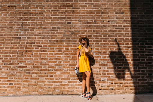 stylish girl with long hair in a yellow dress and sunglasses near the brick wall