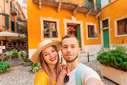 the couple in love take a selfie on the background of the building. girl with boater smiles and looks at the camera. the guy with the beard is also looking into the camera