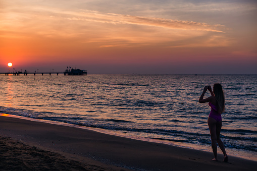 The girl in a swimsuit makes photographs on the phone of the sunset and the sea