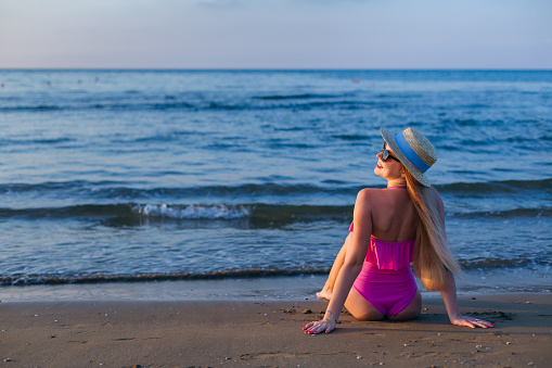 girl sitting on the beach in pink swimsuit and boater