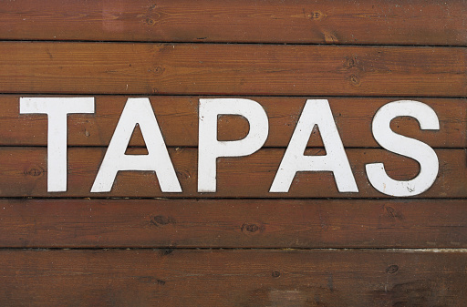 Tapas, an Appetizer or Snack in Spanish Cuisine, White Text on Wooden Background.