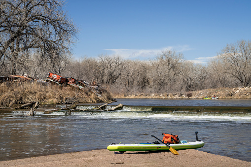 inflatable stand up paddleboard with a paddle, dry bag and action camera on a sandbar below diversion dam, early spring paddling on the South Platte River in Colorado.