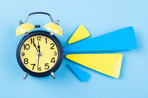 Alarm clock and papers on blue background. The clocks time is showing 5 to 12.