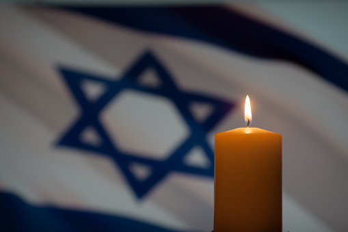 Burning candle on Israel flag background. International Holocaust Remembrance Day, January 27.