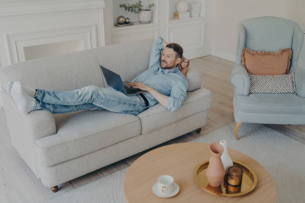 istock Young businessman working remotely at home while lying on couch 1479485225