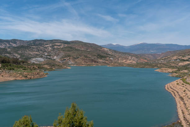 Beninar reservoir in southern Spain, there are trees and bushes, it is a mountainous area, there are clouds in the sky