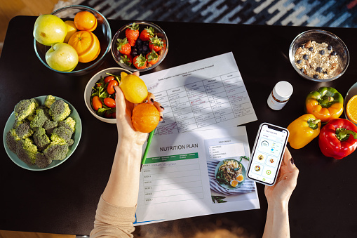 High angle view on a woman checking nutrition value intake via a smartphone diet tracker app. She is holding smart phone with the opened app and fruits.