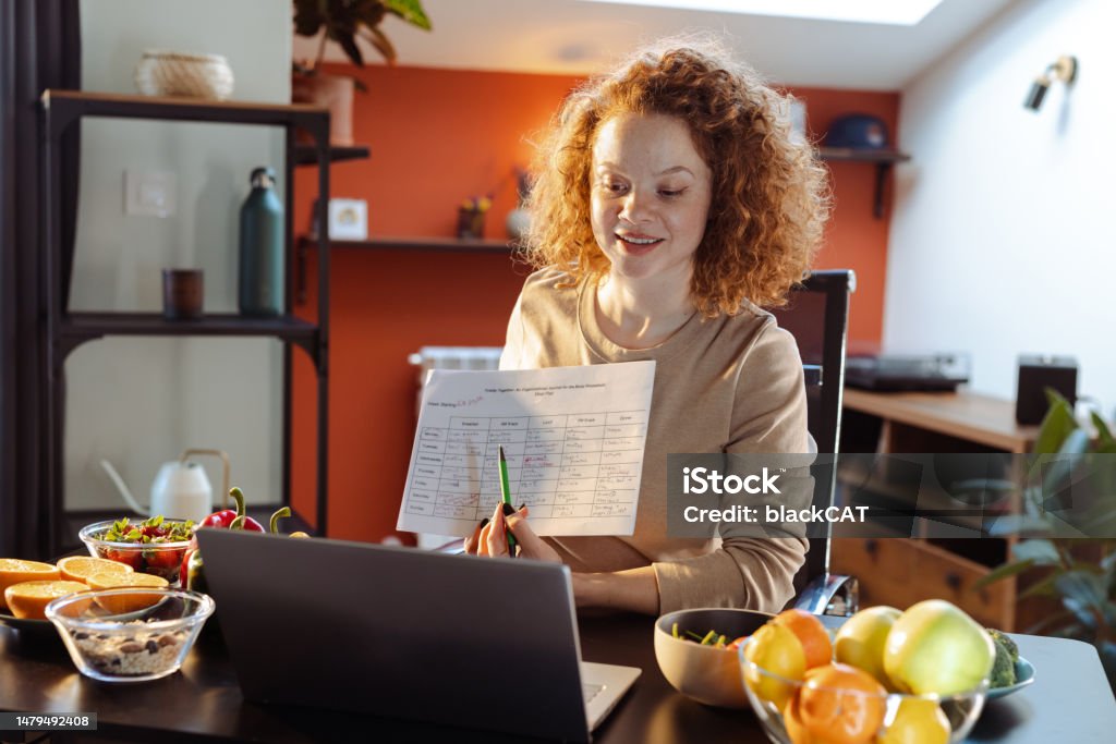 A female dietitian recommending healthy nutrition plan to a client Portrait of a young nutritionist talking online with a client. She is showing a nutrition plan while talking. Nutritionist Stock Photo