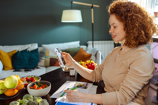 Portrait of a young nutritionist talking online with a client. She is writing a nutrition plan while talking.