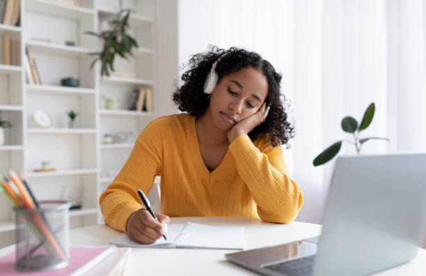 istock Bored young black female student having dull online lesson on laptop computer, writing down information at home 1479493530