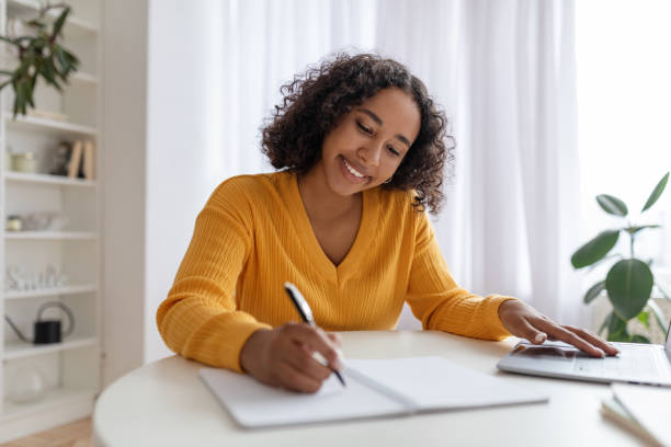 istock Young black woman studying or working online with laptop at home, taking notes, enjoying distance job or education 1479493850