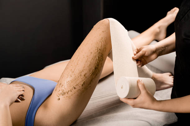 verbandswickelprozess nach dem auftragen von peeling auf die beine des mädchens für styx-wickelung und banding-anti-cellulite-verfahren im spa. masseur macht peeling-massage für die hautreinigung im spa. - torso female hip human skin stock-fotos und bilder