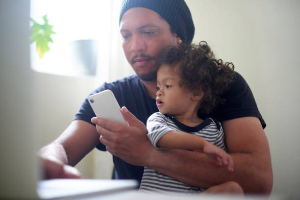 istock Black family, children or multitasking with a single dad and son working on a laptop while holding a phone. Kids, mobile or computer with a busy man and boy child bonding together in their home 1479499029