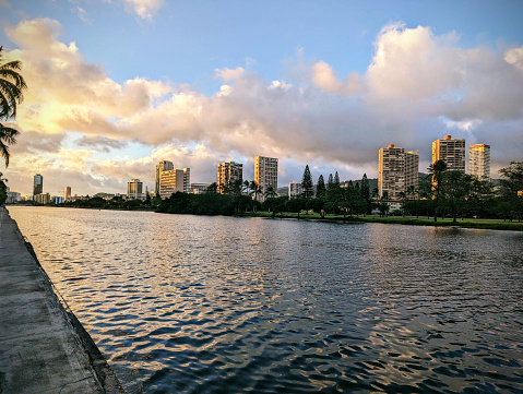 The Ala Wai Canal at Sunset is a beautiful and serene spot to enjoy the sunset over the city of Honolulu. The canal is lined with condos, golf courses, and coconut trees, and in the distance, the mountains of the Ko'olau Range can be seen. This panoramic photo shows the beauty and tranquility of this popular tourist destination.