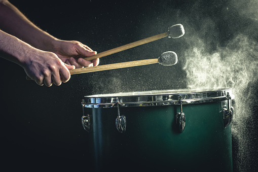 A man plays a musical percussion instrument with sticks on a dark background.