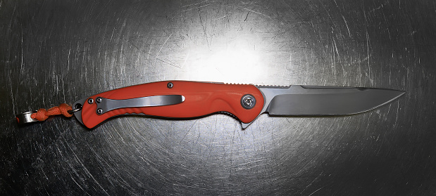 Folding knife with an orange handle on a metal surface close-up