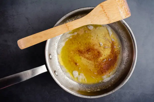 Overhead view of browned butter in a frying pan on a dark background